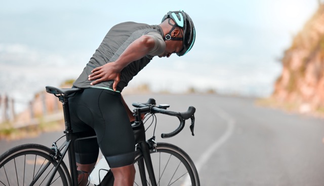 fitness, sports injury and back pain by man cyclist feel uncomfortable while cycling along mountain route. training, pain and injured athletic guy suffering from joint, muscle and spinal discomfort